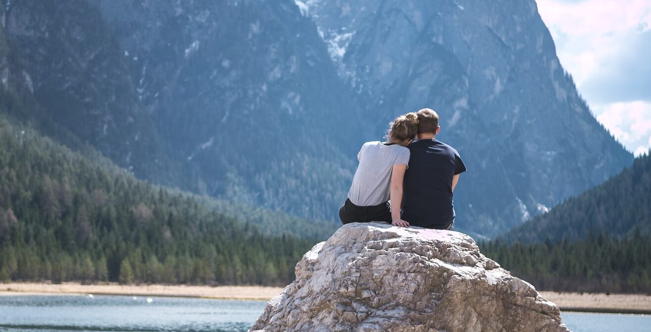 A couple sits closely together enjoying a mountain view.