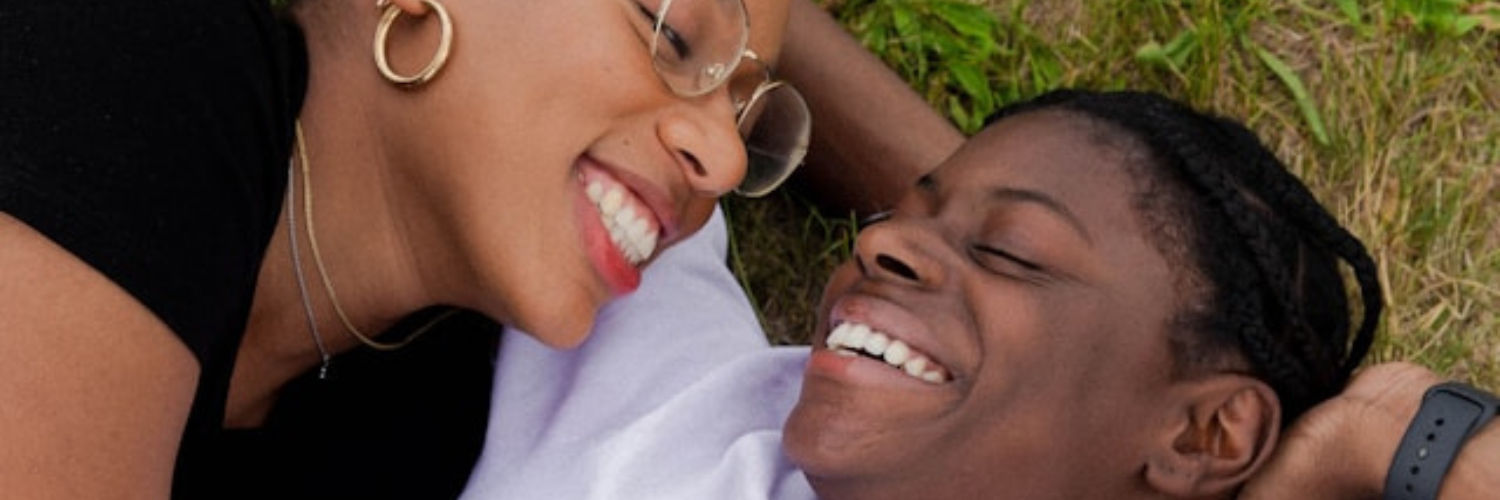 Two partners kissing on the beach, with one laying down and the other hovering over.