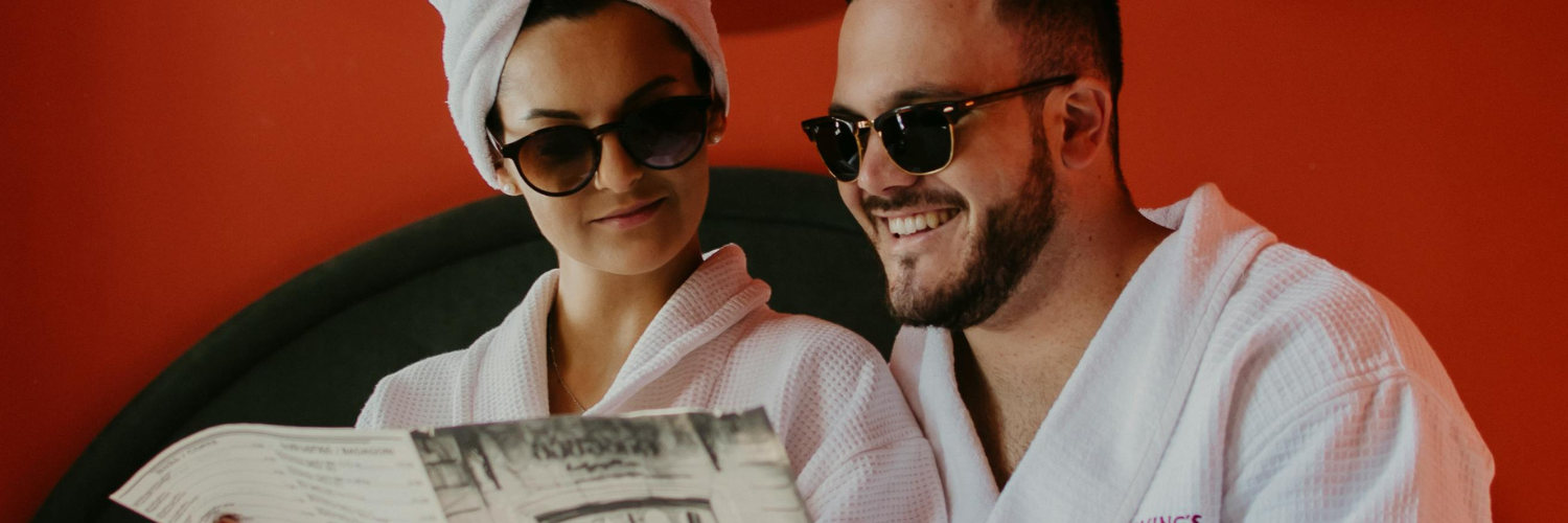 A couple wearing bathrobes and sunglasses, reading a hotel menu.