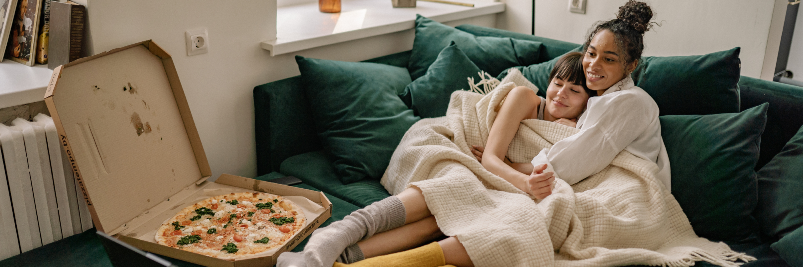 A couple cuddling on the couch with a pizza.