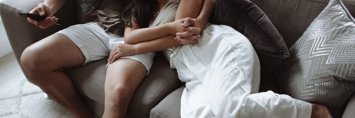 A couple cuddling on the couch with a pizza.